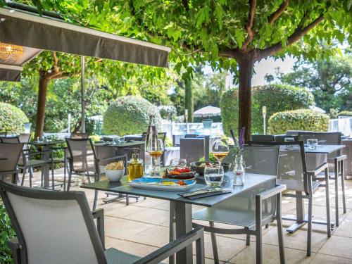 a table and chairs on a patio with trees at Mercure Cavaillon in Cavaillon