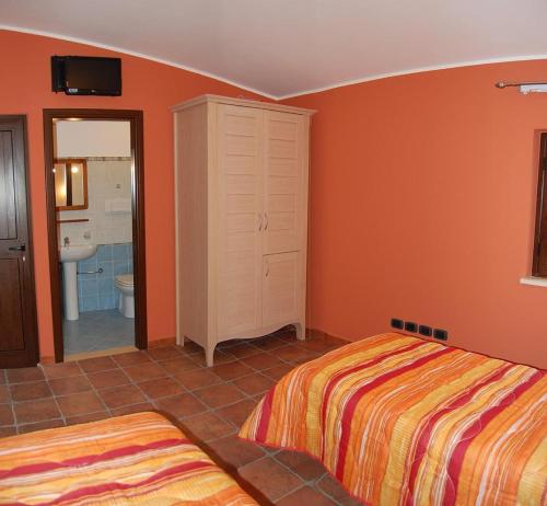 a bedroom with orange walls and two beds and a bathroom at Agriturismo Parra in Santa Lucia del Mela