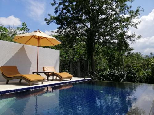 a swimming pool with two chairs and an umbrella at Khaolak Blue Sky Villa in Khao Lak