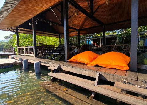 two orange pillows sitting on a wooden table next to water at Baan Rim Nam in Ko Chang