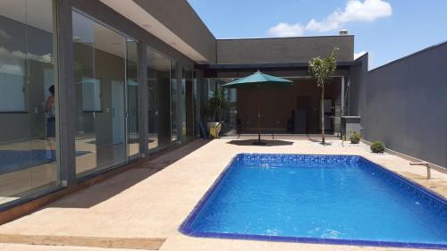 a swimming pool in front of a house with an umbrella at Casa Família Porto in Olímpia