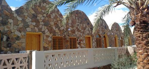 a stone house with a white fence and palm trees at Safari Camp Bahariya Oasis in Bawiti