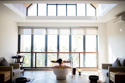 a person in a bath tub in a room with large windows at The Kayana Beach Lombok in Senggigi 