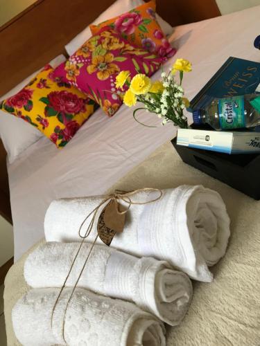 a bed with two rolled towels and a book and flowers at Apto Cond Ilhas do Caribe - Pr - Beira Mar in Matinhos