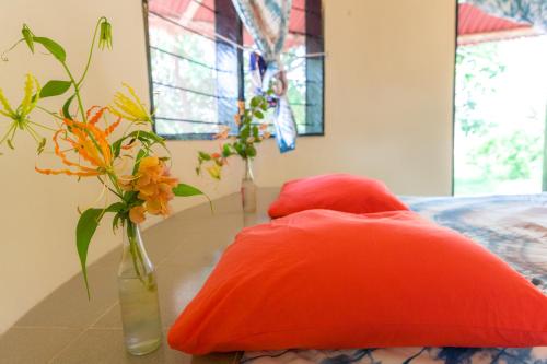 twee oranje kussens en een vaas met bloemen op een tafel bij Tamba Kuruba Eco-lodge in Folonko