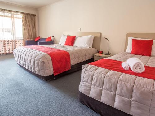 a bedroom with two beds with red and white sheets at ASURE Scenic Route Motor Lodge in Geraldine
