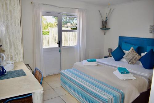 a bedroom with a bed and a table and a window at The Green Palm Cottage in Plettenberg Bay