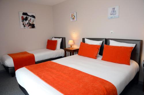 two beds with orange and white pillows in a room at Hôtel Restaurant La Paix La Robe et le Palais in Forges-les-Eaux