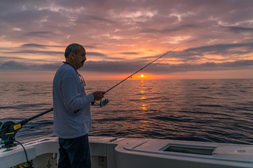a man standing on a boat holding a fishing rod at Villa Experience - Relais Il Termine Elba in Rio Marina