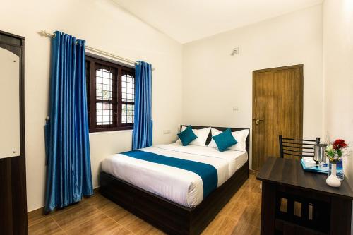a bedroom with a bed with blue curtains and a desk at Wayanad Three Roots Holiday Home Resort in Sultan Bathery
