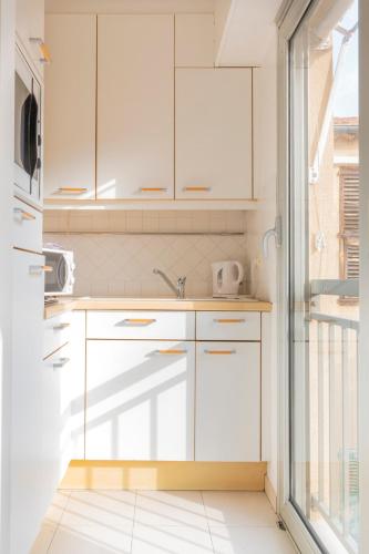 une cuisine avec des armoires blanches et une fenêtre dans l'établissement Studio à deux pas du Palais des Festivals, à Cannes