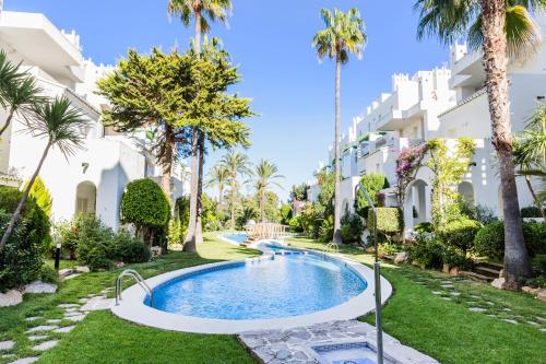 a swimming pool in front of a building with palm trees at Oasis Club II Triplex Apartment by Rock Rentals in Jávea