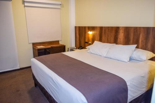 a bedroom with a large white bed with a wooden headboard at Hotel Villa del Carmen in Arequipa