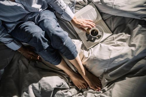 a person laying on a bed with a book and a camera at Boutiquehotel Genusswerk Eifel in Körperich