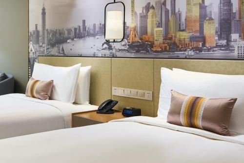 two beds in a hotel room with a picture of a city at The Qube Hotel Shanghai Sanjiagang - Offer Pudong International Airport and Disney shuttle in Shanghai