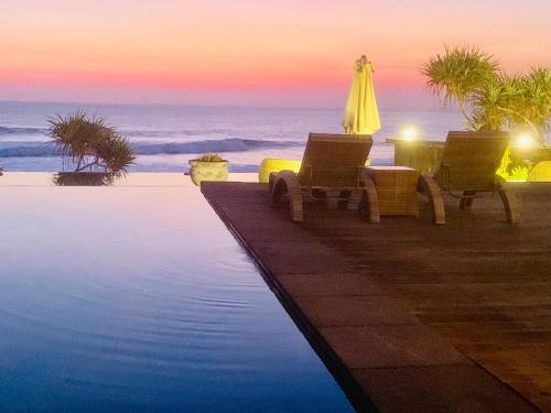 a pool with chairs and an umbrella and the ocean at The Palms Ceningan Hotel in Nusa Lembongan