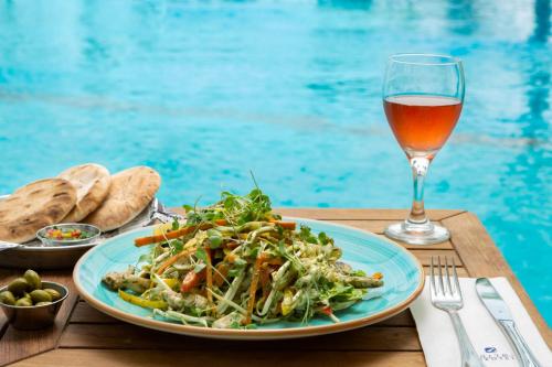a table with a plate of salad and a glass of wine at Nevo by Isrotel Collection in Ein Bokek