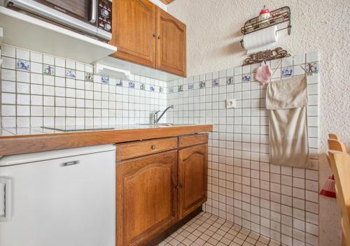 a kitchen with wooden cabinets and a white tiled wall at Résidence L’Etendard in Les Deux Alpes