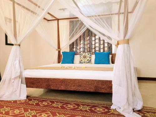 a bedroom with a canopy bed with blue pillows at Villa Oman in Bwejuu