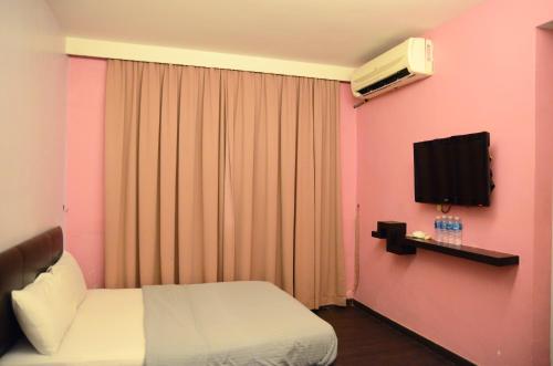 ein Schlafzimmer mit einem Bett und einem TV an einer rosa Wand in der Unterkunft NEWLAND HOTEL in Johor Bahru