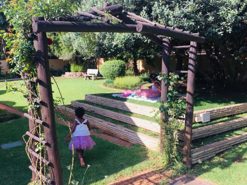 uma menina a caminhar sob um arco de madeira num jardim em Riverton Manor em Centurion