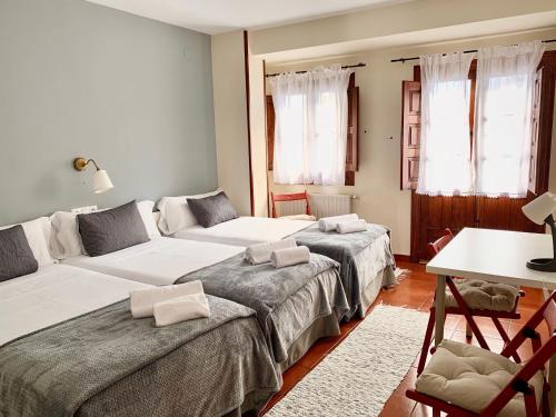 a room with two beds and a table and windows at Hotel Rural Tia Margot in Candelario