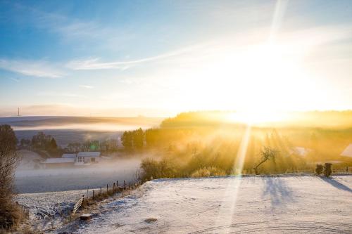 a sunrise over a snowy field with the sun shining at Chateau d'Urspelt in Urspelt