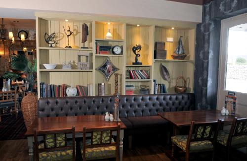 a restaurant with a leather bench and tables and shelves with books at Talardy, St Asaph by Marston’s Inns in St Asaph
