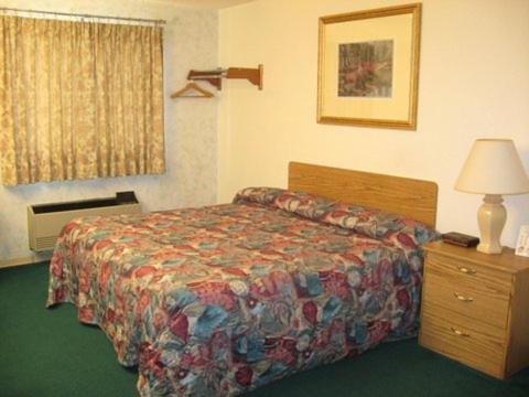 a hotel room with a bed and a lamp and a dresser at Glacier Gateway Inn in Cut Bank