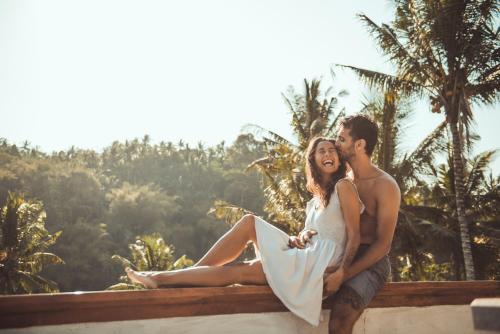 a bride and groom sitting on a wall with palm trees at Dana Bali Ricefield Villa in Candidasa