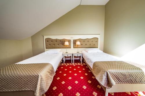 two beds in a room with a red carpet at Hotel Sobienie Królewskie in Sobienie Szlacheckie
