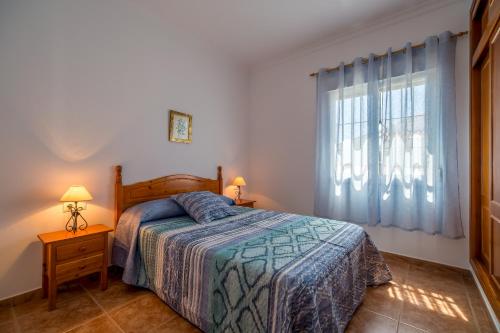 1 dormitorio con 1 cama y una ventana con cortinas azules en Chalet Pedro III, en Conil de la Frontera