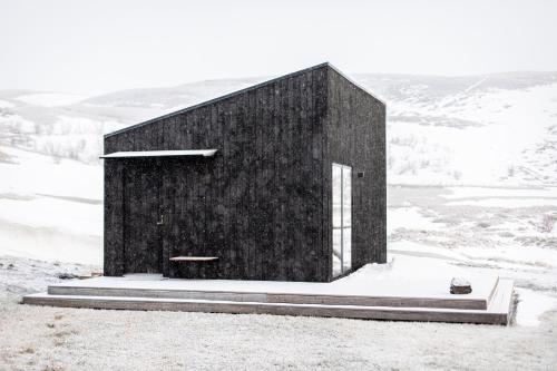 a black building sitting on top of a snow covered hill at Aska, Modern Cabin in Myvatn
