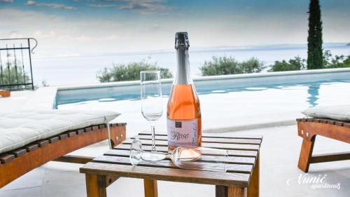 a bottle of wine and glasses on a table next to a pool at Apartments Vunić in Mošćenička Draga