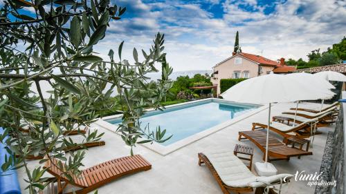 a pool with chairs and an umbrella next to a house at Apartments Vunić in Mošćenička Draga