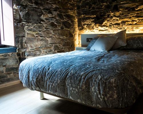 Cama en habitación con pared de piedra en Casa Nastasia, en A Pontenova