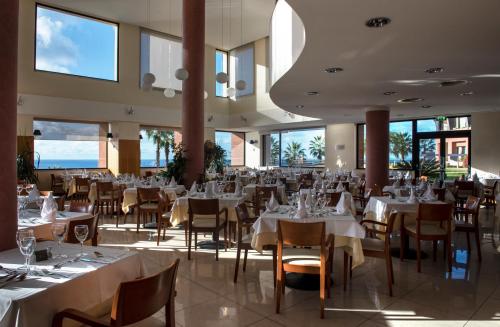 a restaurant with white tables and chairs and windows at Monte Mar Palace Hotel in Ponta Delgada
