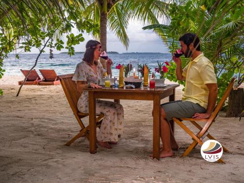 a man and woman sitting at a table on the beach at LVIS blancura Hotel in Dharavandhoo