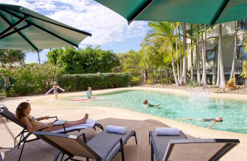 a woman sitting in chairs in a swimming pool at The Retreat Beach Houses in Peregian Beach