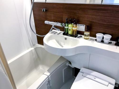 a bathroom with a white sink and a bath tub at HOTEL LiVEMAX Chiba Soga-Ekimae in Chiba