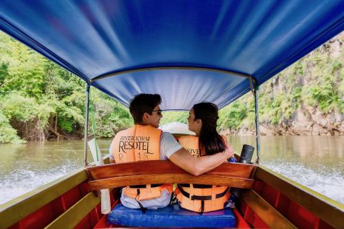 a man and woman sitting on a boat on the river at The Float House River Kwai in Sai Yok