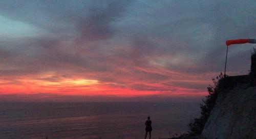 a person standing on top of a cliff with a sunset at The Ulus Klumpu in Uluwatu