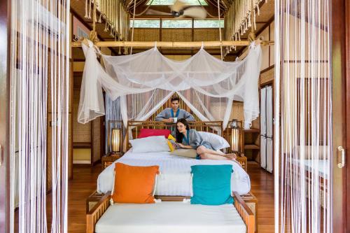 a man and woman sitting on a bed in a room at The Float House River Kwai - SHA Extra Plus in Sai Yok