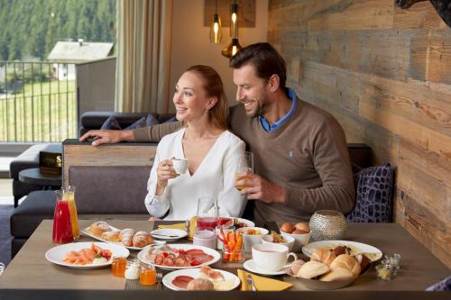 a man and a woman sitting at a table with food at Chalet SALENA luxury lodge in Santa Maddalena in Casies