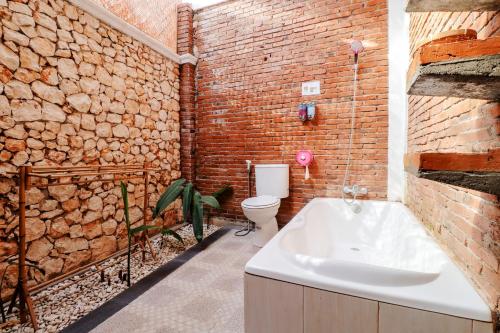 a brick bathroom with a tub and a toilet at Omah Teras Bata Guesthouse in Yogyakarta