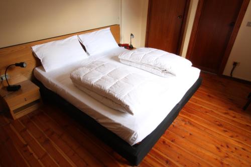 un letto con lenzuola e cuscini bianchi su un pavimento in legno di Hotel Adamello a Temù