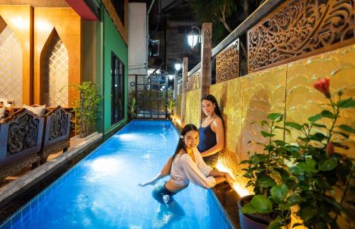 two women sitting on the edge of a swimming pool at Tepbunthom Hostel in Bangkok