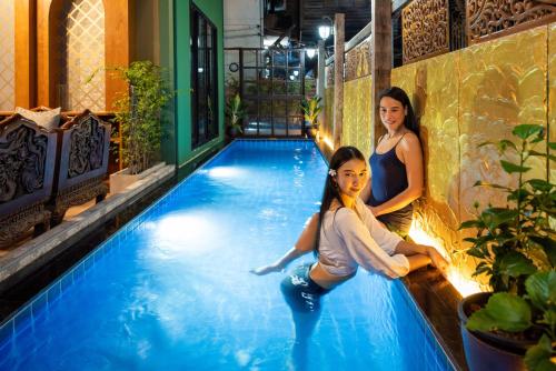 two women are sitting in a swimming pool at Tepbunthom Hostel in Bangkok