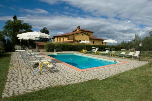 a swimming pool with chairs and umbrellas in front of a house at Il Bellini in Castelfranco di Sopra