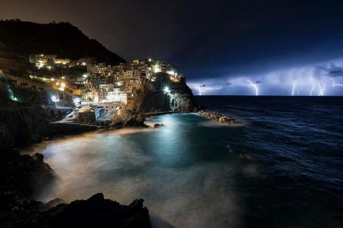 a lightning storm over a beach with a city at night at Ines Apartment in Manarola